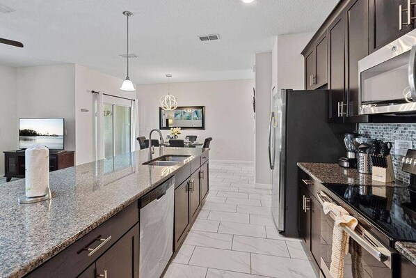 A modern kitchen with granite countertops, stainless steel appliances, and a dining area with a view. - SL3095 - 4BR house with pool near Disney parks (Kissimmee)