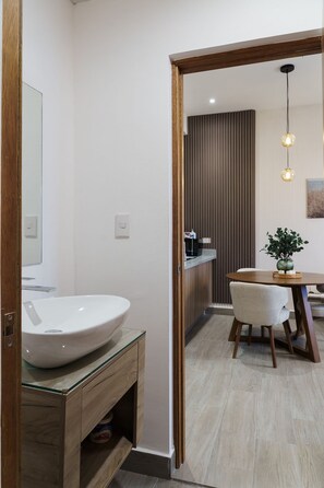A modern bathroom with a large white sink, wooden vanity, and a dining area with a table and chairs.
