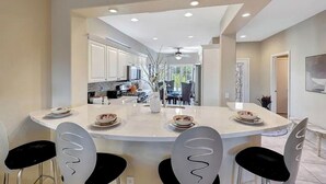 Uma cozinha moderna com ilha central, armários brancos e cadeiras pretas.