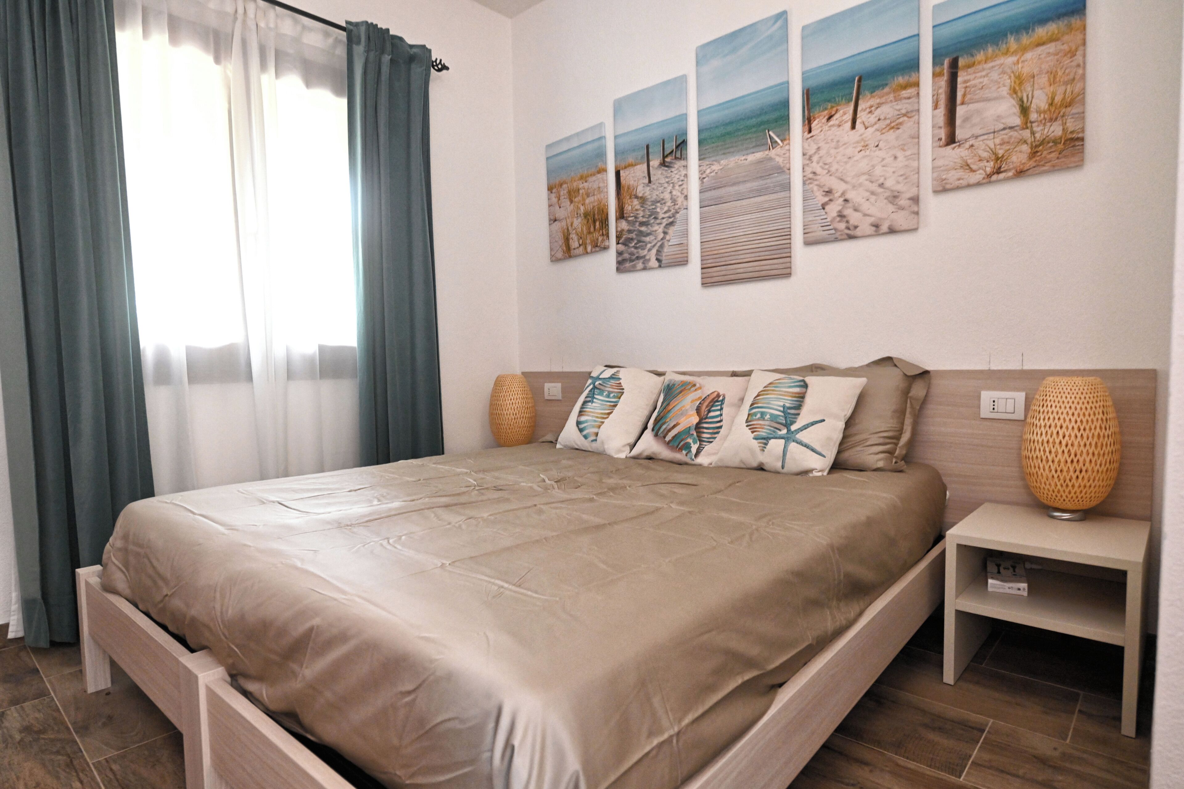 A bedroom with a bed, a nightstand, and a wall with three beach-themed paintings.