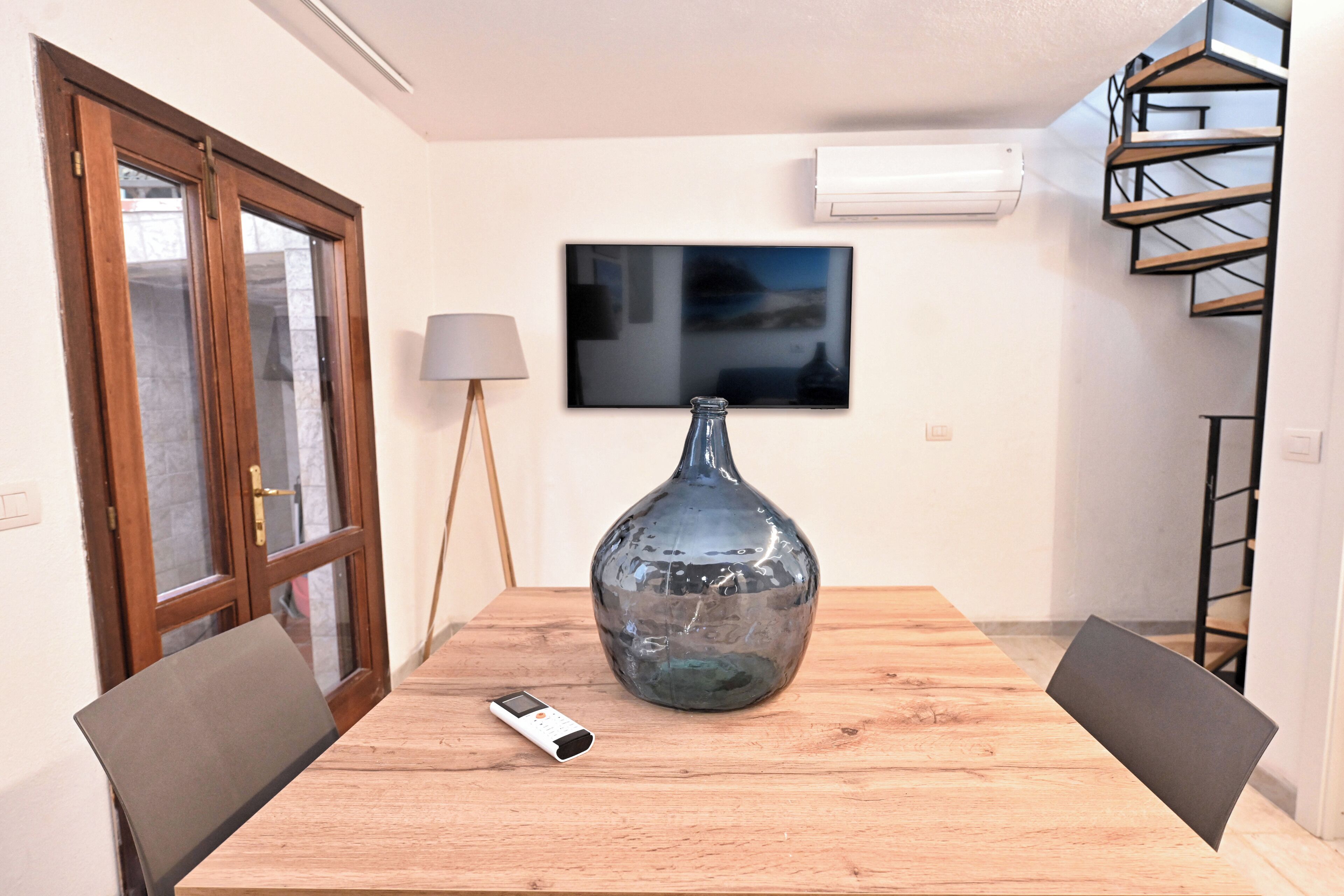 A dining table with a large vase, a remote control, and a television on the wall.