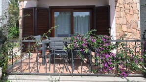 Un espace extérieur abrité, avec une table et des chaises, un mur en pierre et une vue sur la rue.