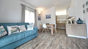 Un salon moderne avec un canapé bleu, une table à manger avec des chaises et un coin cuisine équipé de placards et d’un évier.