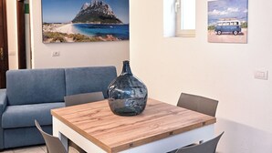 Une pièce avec une table en bois, un canapé bleu et un grand tableau représentant une plage et des montagnes.