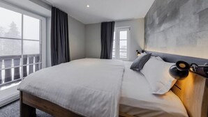 Un dormitorio moderno con una cama grande, un cabecero con una lámpara y vistas al exterior a través de una ventana.