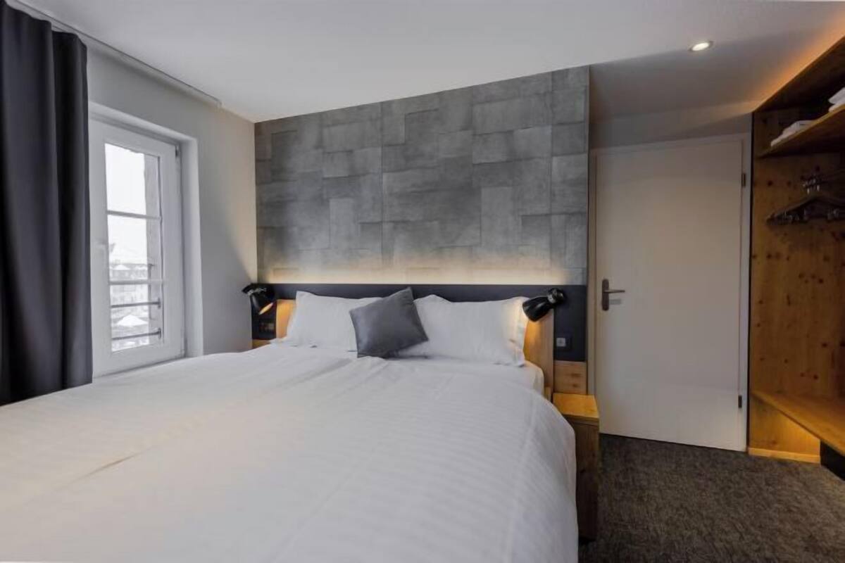 Une chambre d’hôtel avec un grand lit, une tête de lit en pierre, une armoire et une fenêtre avec des rideaux.