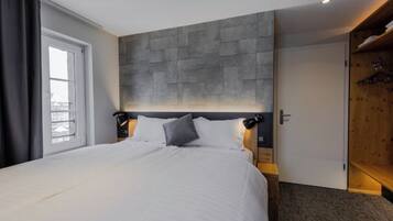 Une chambre d’hôtel avec un grand lit, une tête de lit en pierre, une armoire et une fenêtre avec des rideaux.