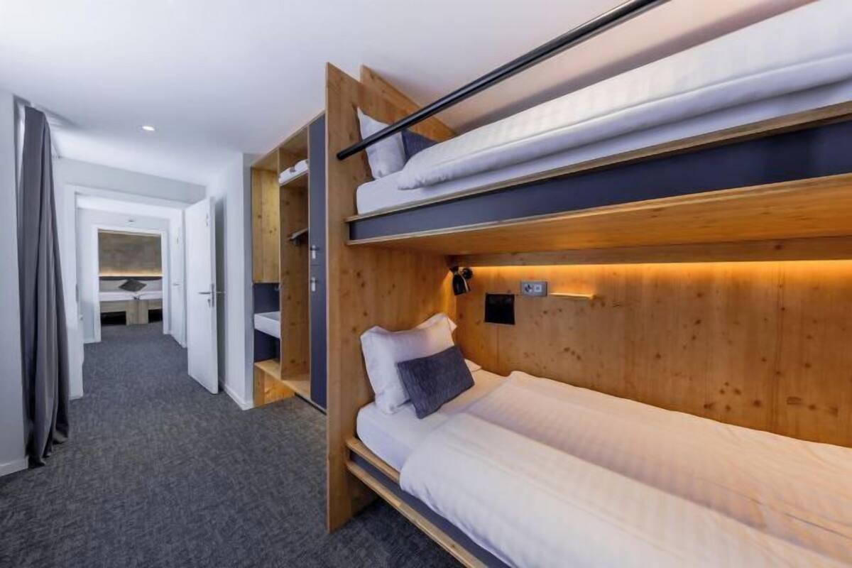 Une chambre avec un lit superposé, une tête de lit en bois, une table de chevet et une lampe fixée au mur.