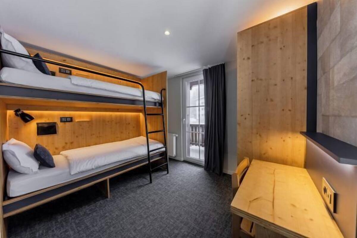 Une chambre avec des lits superposés, un bureau, une fenêtre avec des rideaux et un mur en bois.