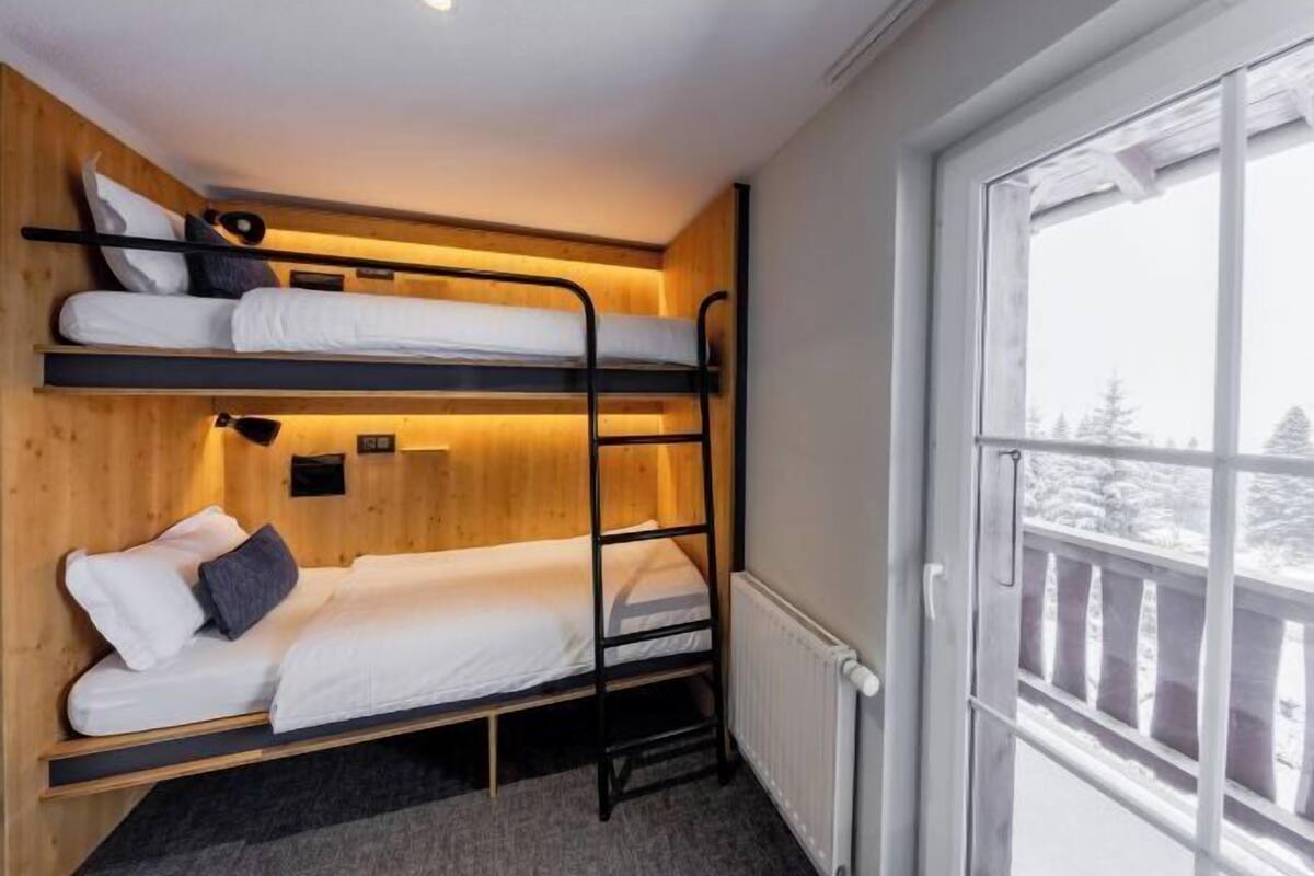 Une chambre avec un lit superposé, une fenêtre, des murs en bois et un radiateur.