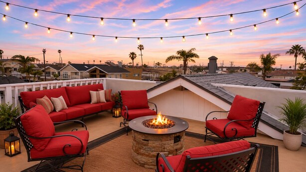 A rooftop patio with a fire pit, red furniture, string lights, and a view of the cityscape.