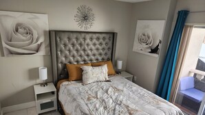 Een slaapkamer met een gestoffeerd hoofdeinde, een bed met een Parijse dekbedovertrek, twee nachtkastjes met lampen, en een groot raam met gordijnen.