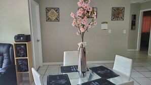 Een eethoek met een glazen tafel, witte stoelen en een vaas met roze bloemen.