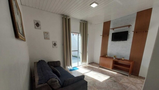 A living room with a sofa, a TV mounted on the wall, and a sliding door leading to a bathroom. - Casa mobiliada (Marituba)
