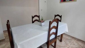 A dining area with a table covered by a white tablecloth, two wooden chairs, a potted plant, and a colorful painting on the wall. - Casa mobiliada (Marituba)