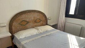 Un lit avec une tête de lit en osier, des oreillers blancs et une couvre-lit à rayures.