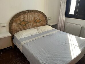 Un lit avec une tête de lit en osier, des oreillers blancs et une couvre-lit à rayures.