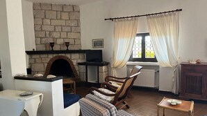 Un salon avec une cheminée en pierre, un téléviseur, un canapé, un fauteuil et une petite table.