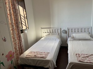 Ein Zimmer mit zwei Einzelbetten, einem Vorhangfenster und einer Wand mit Blumenmuster.