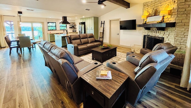 A spacious living room with a long leather sofa, a dining area with a wooden table, and a stone fireplace. - Gated Lake Ranch, Private Dock & 3.5 Acres, Fire pit & Pet Friendly (Palo Pinto)
