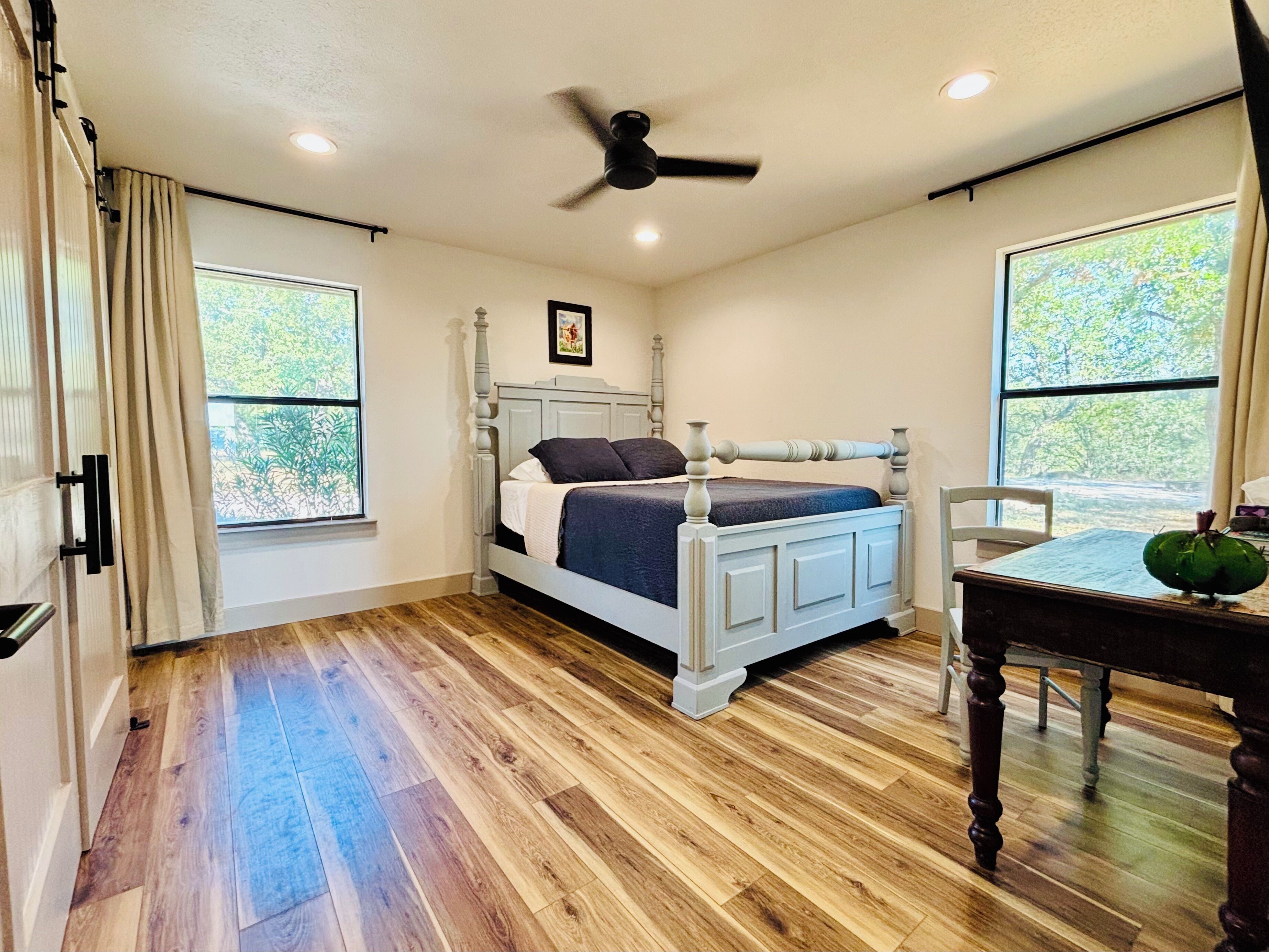 A bedroom with a bed, a ceiling fan, a window, and a wooden floor.
