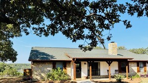 A stone house with a covered porch, a chimney, and a view of a lake. - Gated Lake Ranch, Private Dock & 3.5 Acres, Fire pit & Pet Friendly (Palo Pinto)