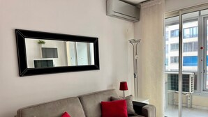 Una sala de estar moderna con un sofá gris, cojines rojos, un espejo grande y un equipo de aire acondicionado.