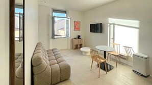 A modern living room with a sofa, a dining table with chairs, a TV, and a window with a view. - Viva Riviera Design and Sunny Commandant André (Cannes)