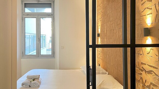 A hotel room with a bed, a window with a view, and a textured wall with wall sconces. - Viva Riviera Design and Sunny Commandant André (Cannes)
