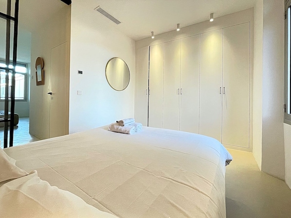A bedroom with a large bed, a wardrobe, a round mirror, and a window.