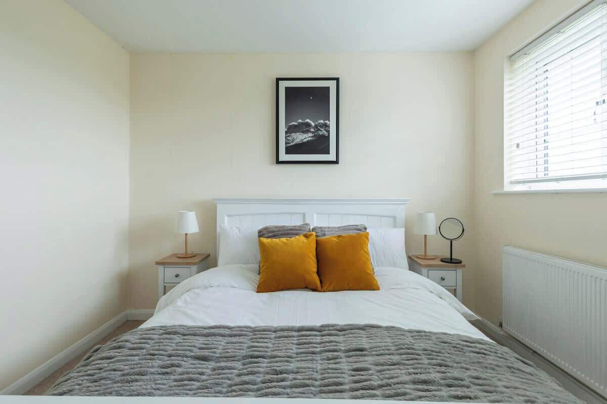 Une chambre à coucher comprenant un lit, deux tables de chevet, une commode, un tableau encadré au mur et une fenêtre avec des stores.