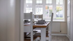 Ruokailutila, jossa on kahdelle katettu pöytä, valkoiset tuolit ja ikkuna, jossa on sälekaihtimet.