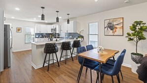 A modern kitchen with white cabinets, a central island, and bar stools. There is a dining table with blue chairs.