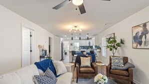 A spacious living room with a sofa, armchairs, a coffee table, and a dining area in the background.
