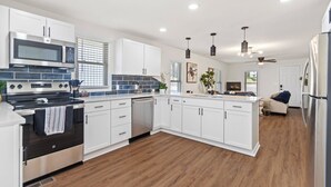 A modern kitchen with white cabinets, stainless steel appliances, and a wooden floor. - Your HOME when you're in Benton! (Benton)