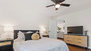 A bedroom with a bed, a television, a ceiling fan, and a nightstand with a lamp.