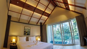 Une chambre avec un grand lit, deux tables de chevet avec des lampes, un tableau au mur et une grande fenêtre donnant sur un paysage verdoyant.