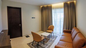 Un salon moderne avec un canapé en cuir marron, une petite table blanche, deux chaises et une porte en bois foncé.