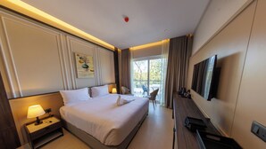 Une chambre d’hôtel avec un grand lit, une table de chevet avec une lampe, un téléviseur à écran plat fixé au mur et une fenêtre avec des rideaux.