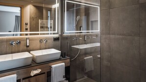 Un baño moderno con dos lavamanos, ducha con cerramiento de vidrio e iluminación integrada en un espejo grande.