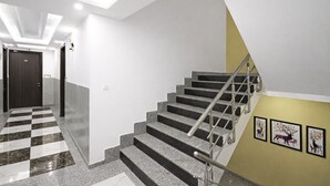 A modern interior with a checkered floor, a staircase with metal railings, and framed artwork on the wall. - 99 Hotel Apple Park (New Delhi)