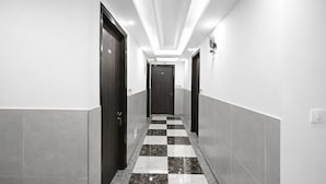 A hallway with checkered flooring, dark doors, and a ceiling light fixture. - 99 Hotel Apple Park (New Delhi)
