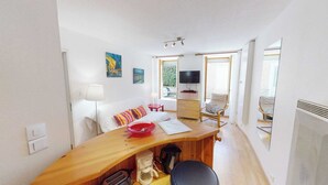 Une petite pièce comprenant un lit, un bureau, une chaise, un téléviseur et une fenêtre.