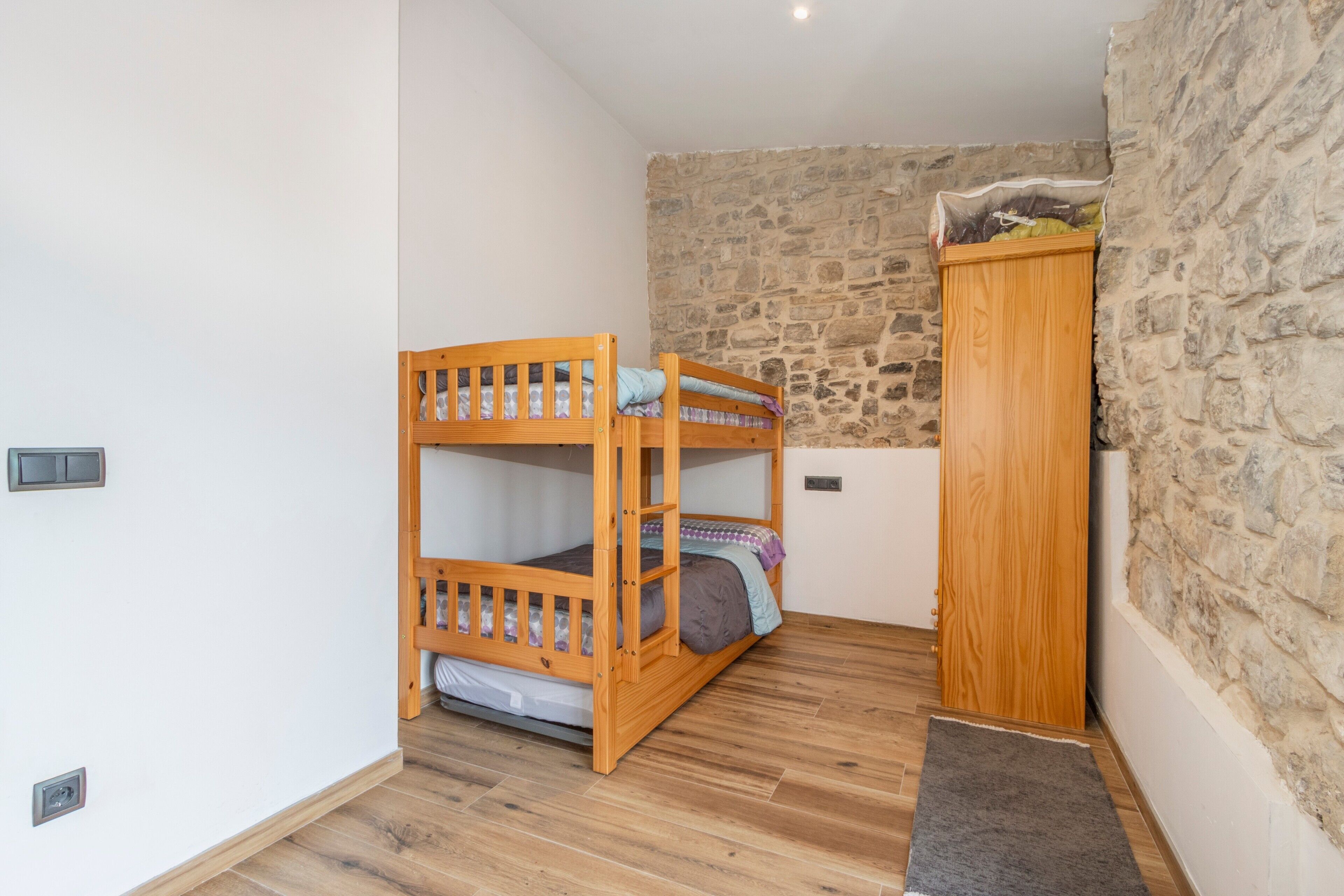 A bunk bed with a wooden wardrobe and a stone wall.