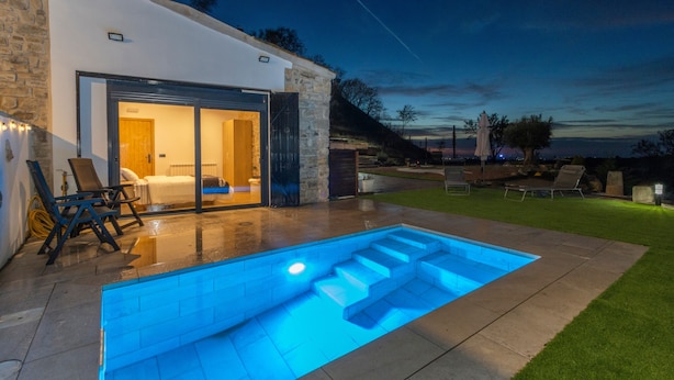 Een modern huis met een zwembad, terras en een stenen muur.