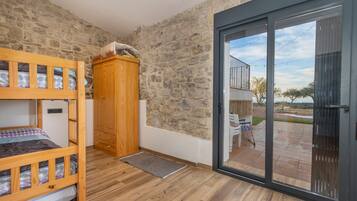 Una habitación con literas, un armario de madera, pared de piedra y una puerta corrediza de vidrio que da a un espacio exterior.