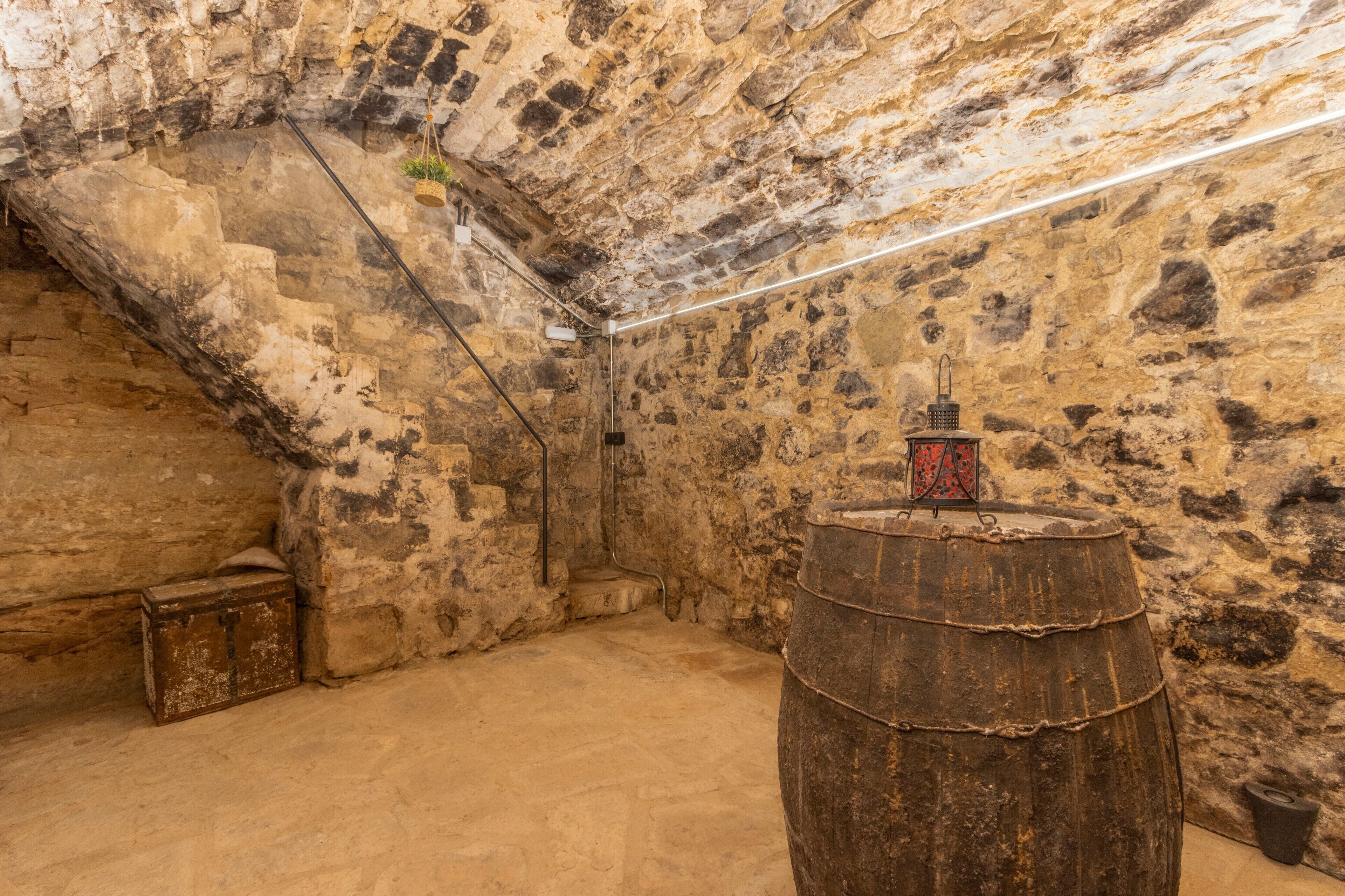 Une pièce aux murs de pierre, avec un tonneau en bois, une petite boîte en bois et une lanterne en métal posée sur un support.