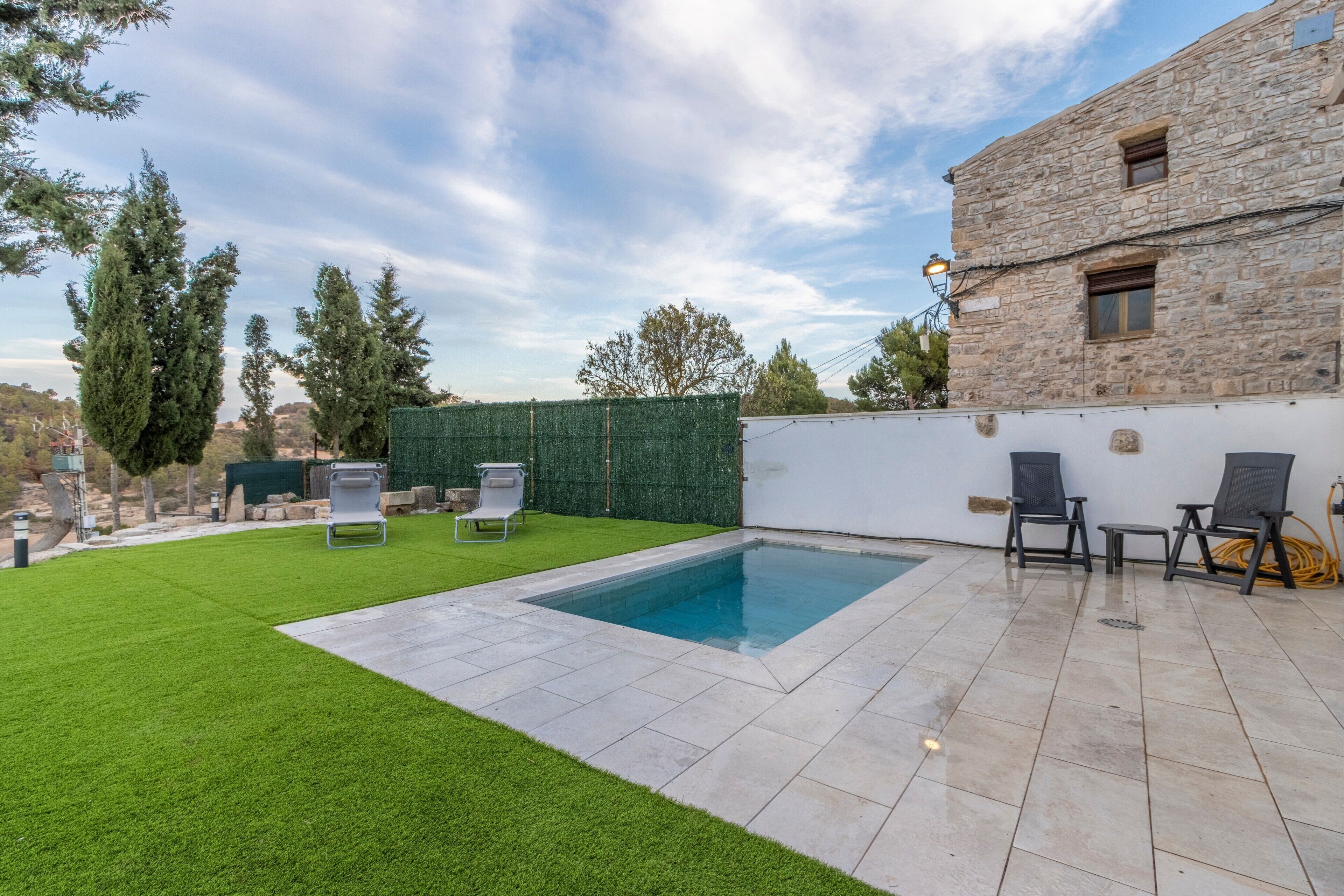Ein Garten mit Swimmingpool, einem Steinhaus und einem grünen Rasen.