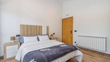 A bedroom with a wooden headboard, a bed with white bedding, a nightstand with a lamp, a wooden door, and a radiator.
