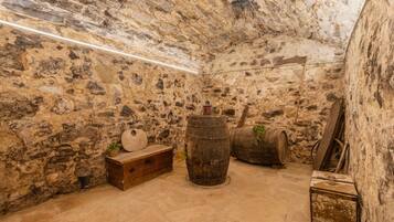 Una habitación con paredes de piedra, un banco de madera, dos barriles y una caja de herramientas.